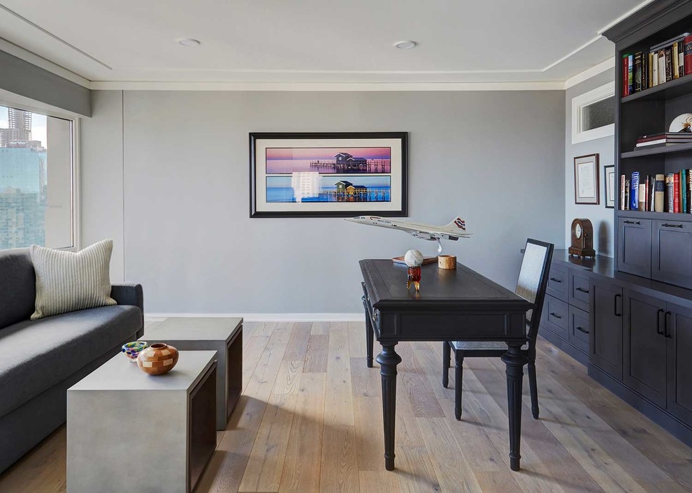Mittelgroßes Modernes Arbeitszimmer ohne Kamin mit Arbeitsplatz, grauer Wandfarbe, hellem Holzboden, freistehendem Schreibtisch und braunem Boden