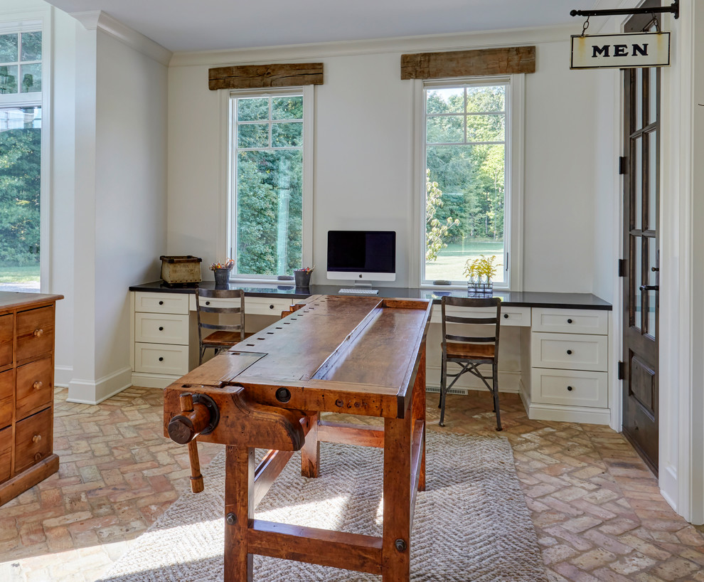Foto de estudio de estilo de casa de campo grande sin chimenea con paredes blancas, suelo de ladrillo, escritorio empotrado y suelo beige