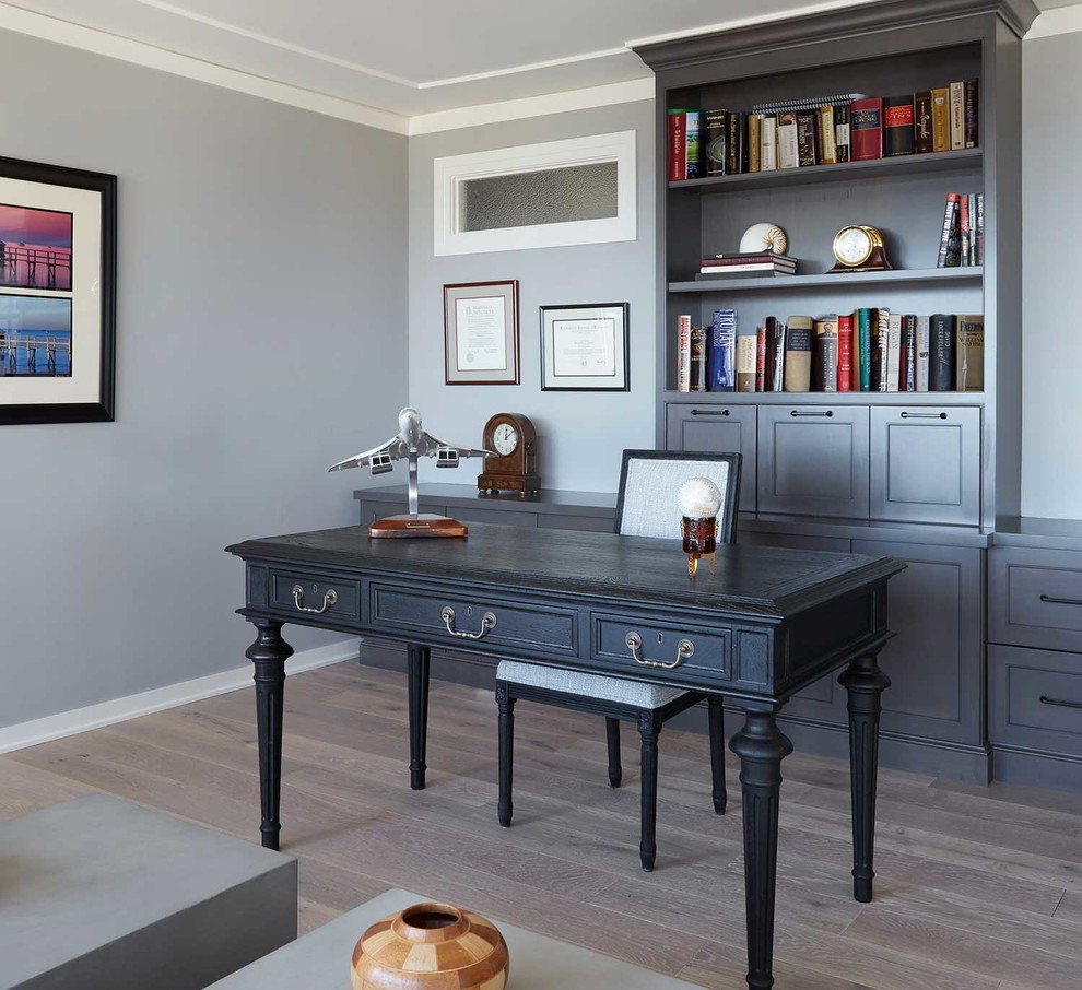 Modelo de despacho actual de tamaño medio sin chimenea con paredes grises, suelo de madera clara, escritorio independiente y suelo marrón