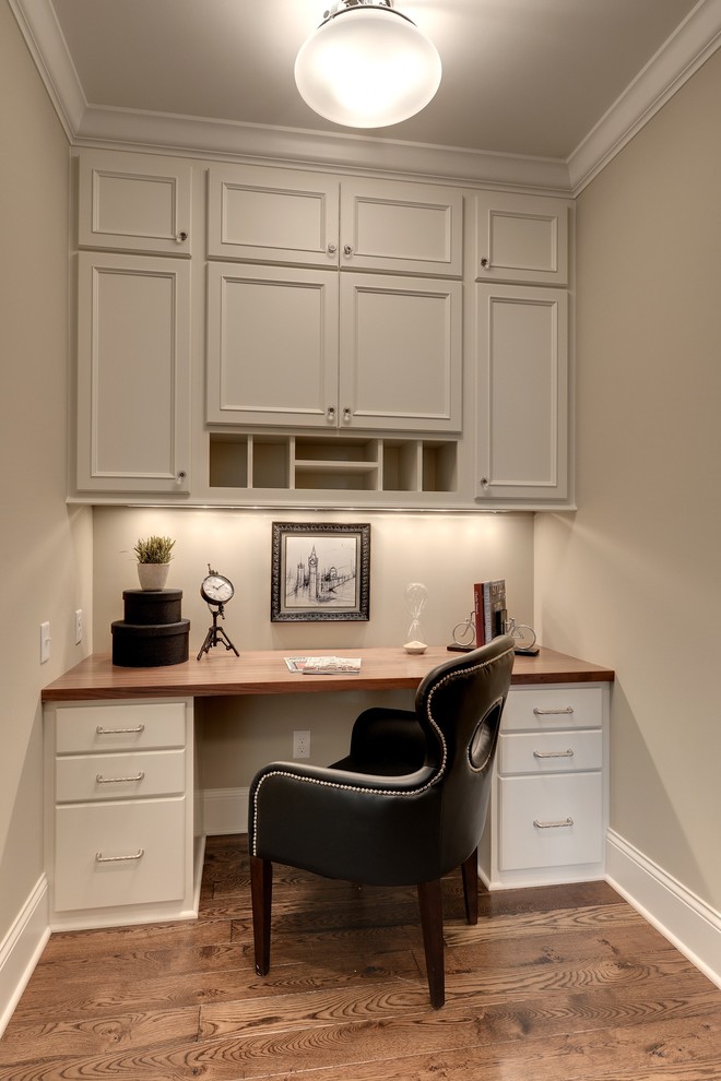 Cette image montre un petit bureau avec un mur beige, un sol en bois brun et un bureau intégré.