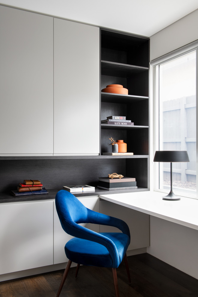 Diseño de despacho actual grande con paredes blancas, suelo de madera oscura, escritorio empotrado y suelo negro