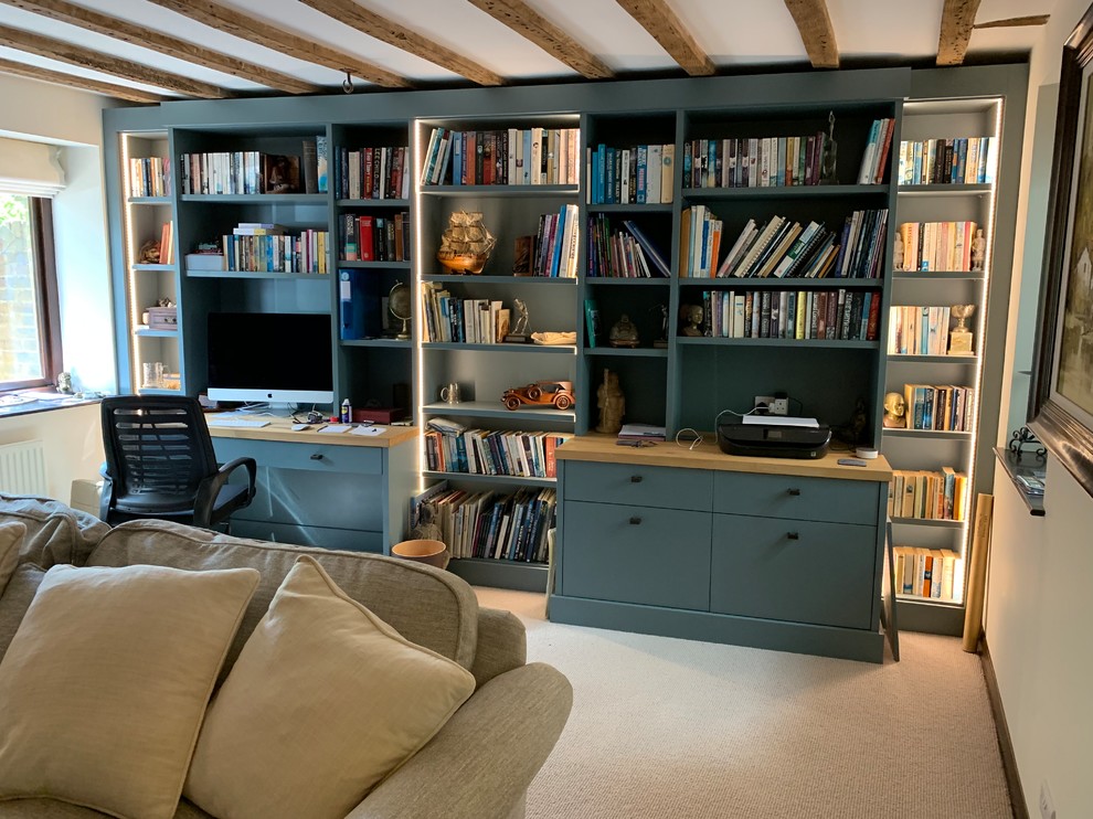 Inredning av ett modernt stort hemmabibliotek, med beige väggar, heltäckningsmatta, en hängande öppen spis, en spiselkrans i tegelsten, ett inbyggt skrivbord och beiget golv