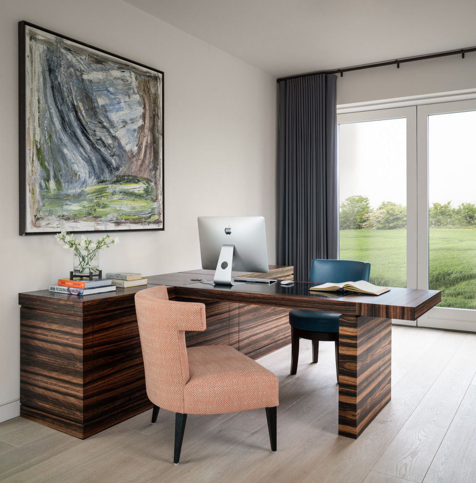 Modelo de despacho actual de tamaño medio con paredes blancas, suelo de madera clara, escritorio empotrado y suelo beige