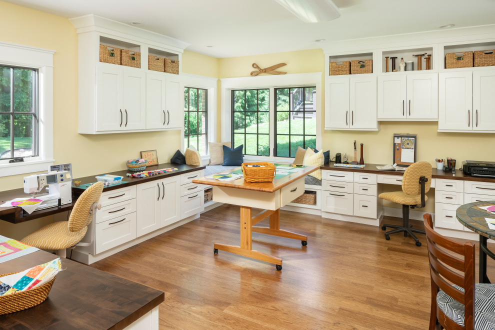 Ejemplo de despacho tradicional grande sin chimenea con paredes amarillas, suelo de madera en tonos medios, escritorio empotrado y suelo beige