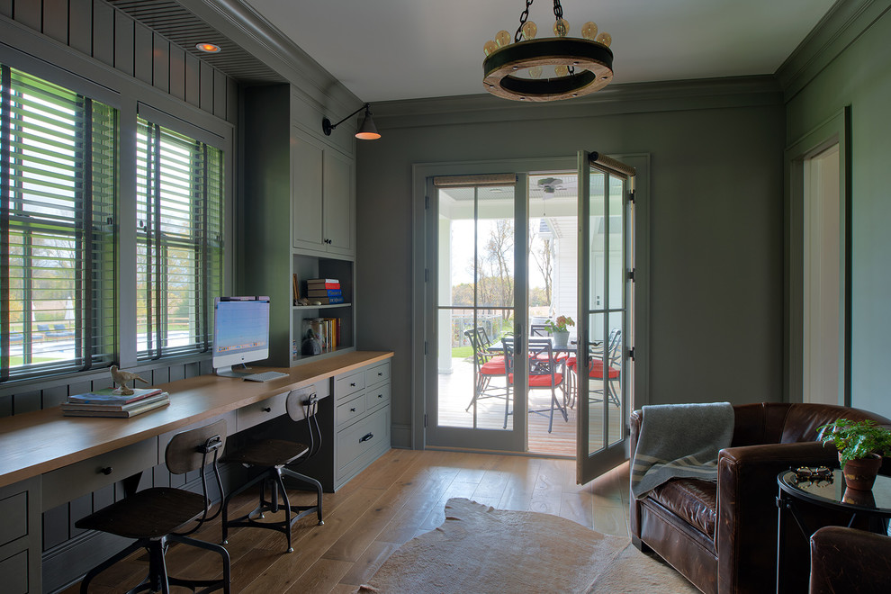 Diseño de despacho de estilo de casa de campo con paredes verdes, suelo de madera clara, escritorio empotrado y suelo marrón