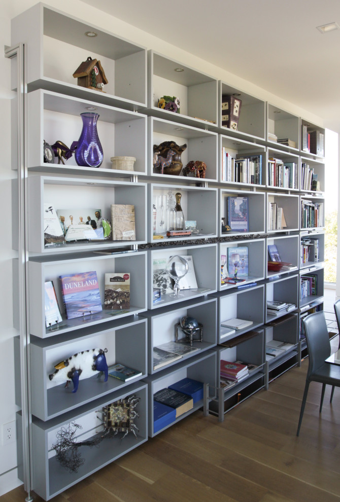 Modelo de despacho minimalista grande con biblioteca, paredes blancas, suelo de madera clara y escritorio independiente