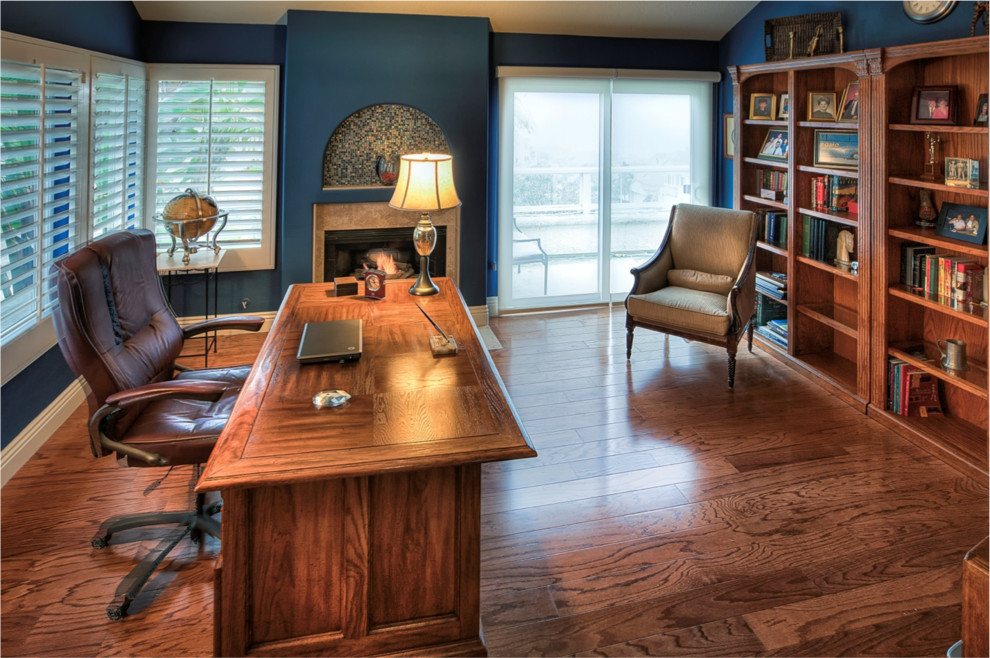 Großes Mediterranes Arbeitszimmer ohne Kamin mit Arbeitsplatz, blauer Wandfarbe, braunem Holzboden und freistehendem Schreibtisch in Orange County