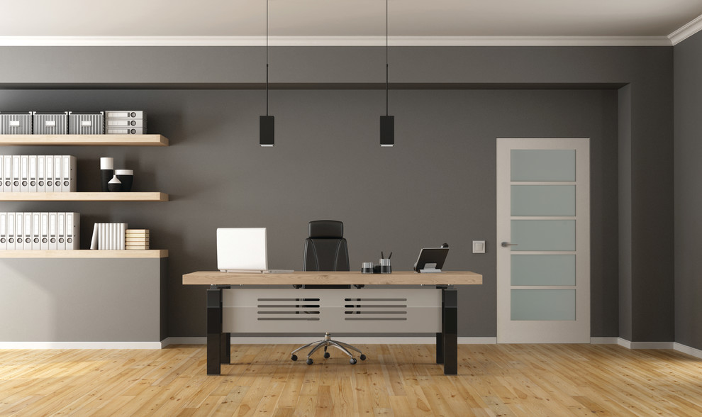 Diseño de despacho actual grande sin chimenea con paredes grises, suelo de madera clara, escritorio independiente y suelo marrón