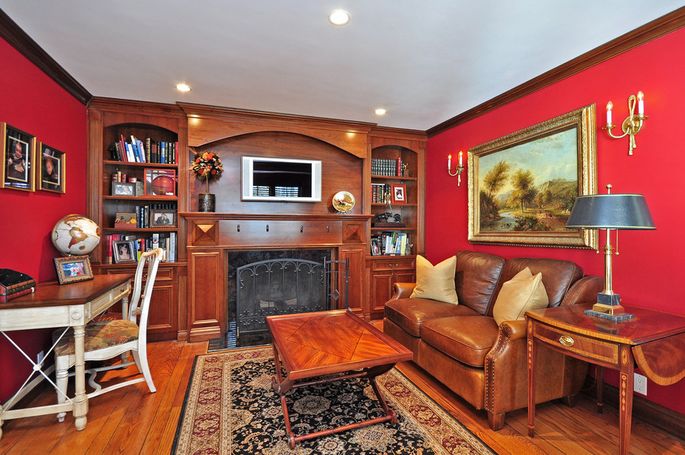 Diseño de despacho clásico con paredes rojas, suelo de madera en tonos medios, marco de chimenea de piedra y escritorio independiente