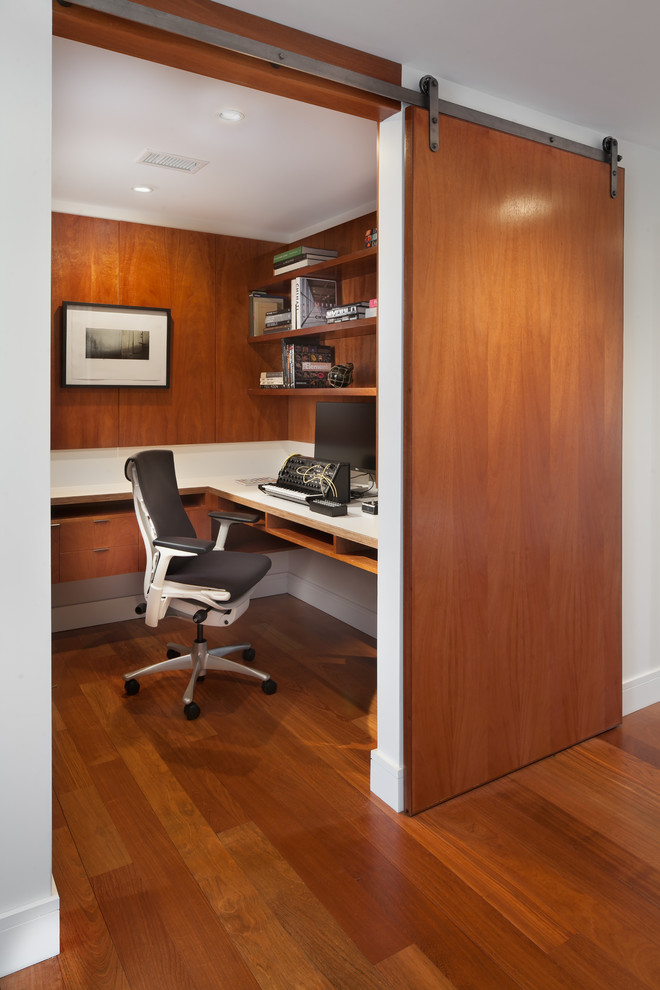 Immagine di uno studio minimal con pareti bianche, pavimento in legno massello medio, scrivania incassata e pavimento marrone