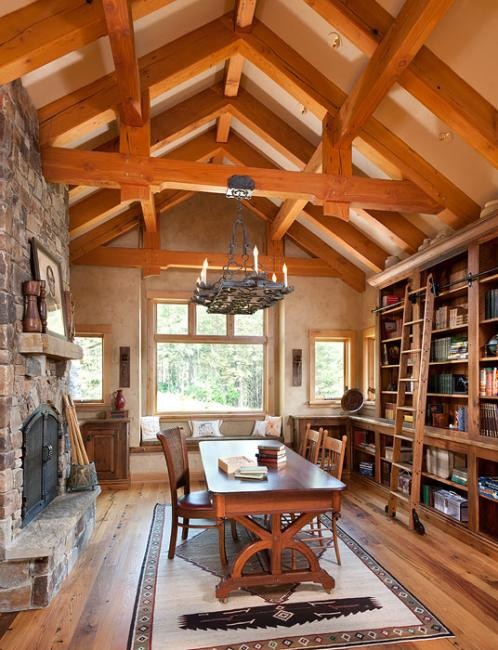 Aménagement d'un grand bureau montagne avec une bibliothèque ou un coin lecture, un mur beige, un sol en bois brun, une cheminée standard, un manteau de cheminée en pierre, un bureau indépendant et un sol marron.