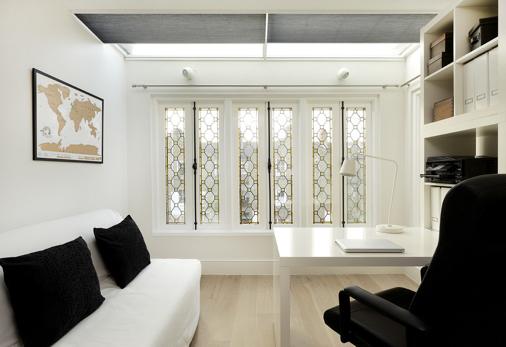 Ejemplo de despacho actual de tamaño medio con paredes blancas, suelo de madera clara y escritorio independiente