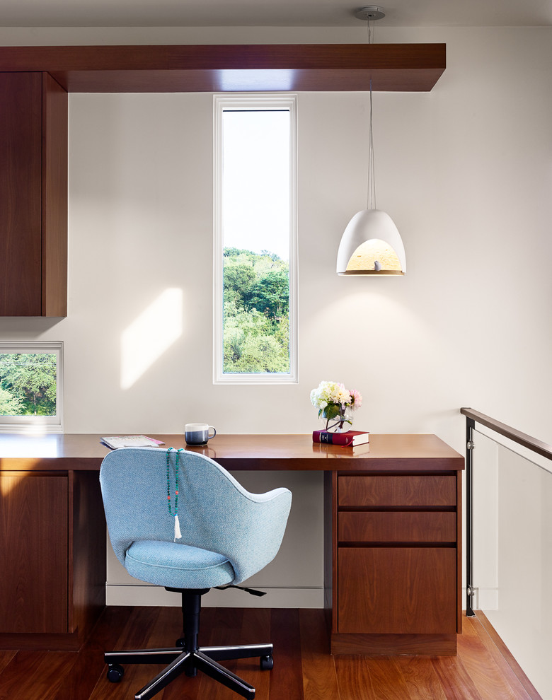 Réalisation d'un bureau design avec un mur blanc, un sol en bois brun et un bureau intégré.