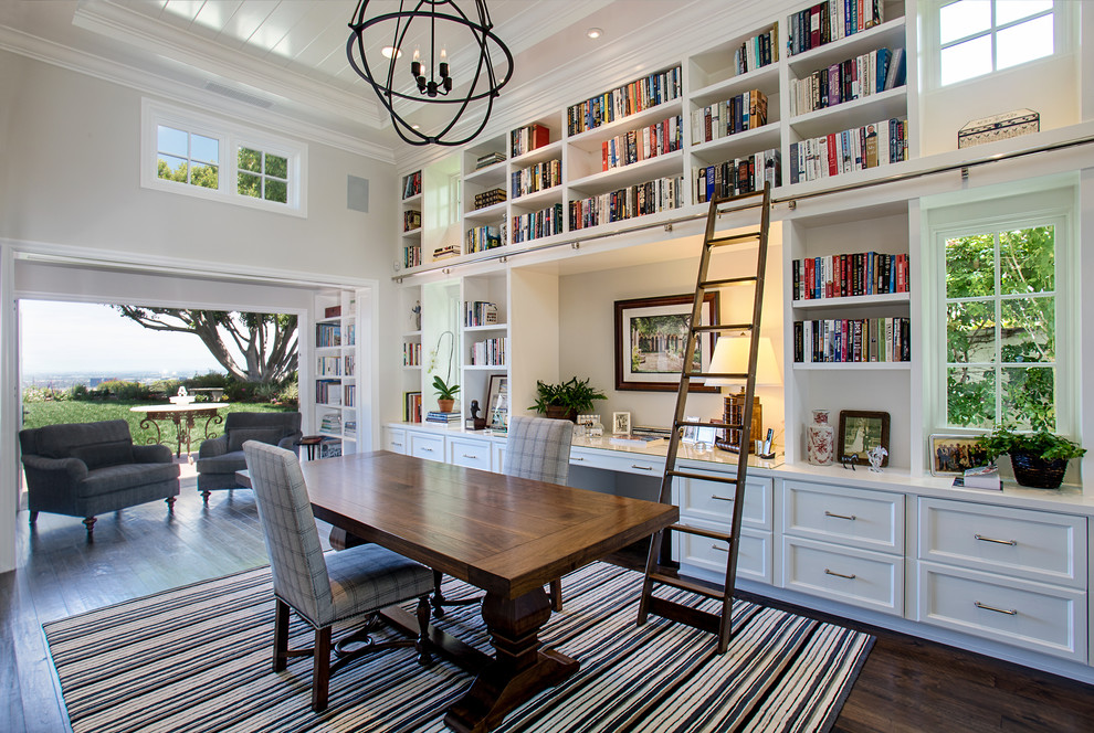 Elegant freestanding desk dark wood floor and brown floor home office library photo in Orange County with white walls