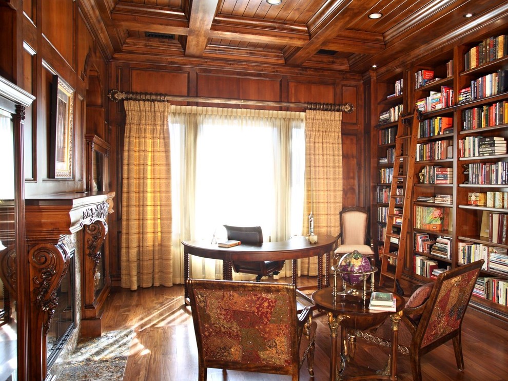 Imagen de despacho mediterráneo extra grande con biblioteca, paredes marrones, suelo de madera en tonos medios, todas las chimeneas, marco de chimenea de madera, escritorio independiente y suelo marrón