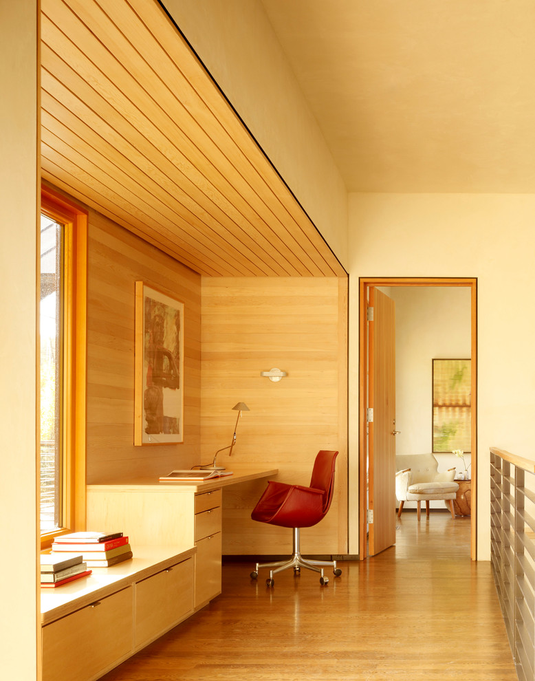 Modern inredning av ett arbetsrum, med beige väggar, mellanmörkt trägolv, ett inbyggt skrivbord och beiget golv