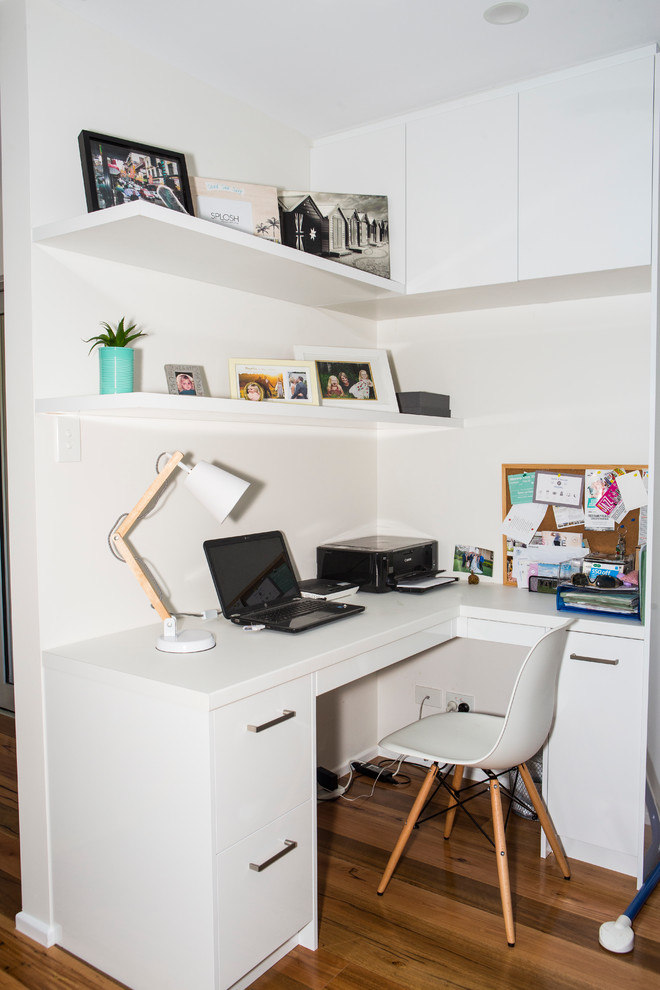 Foto på ett litet funkis hemmabibliotek, med vita väggar, ljust trägolv och ett inbyggt skrivbord