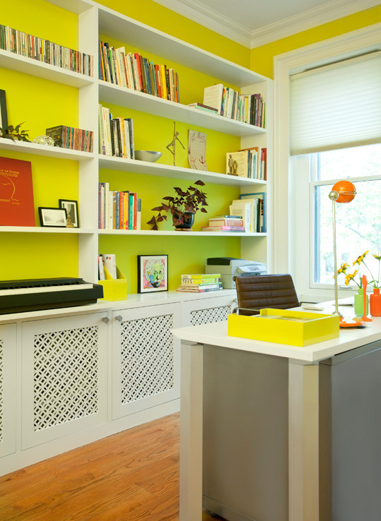 Modern inredning av ett mellanstort hemmabibliotek, med gula väggar, ljust trägolv och ett fristående skrivbord