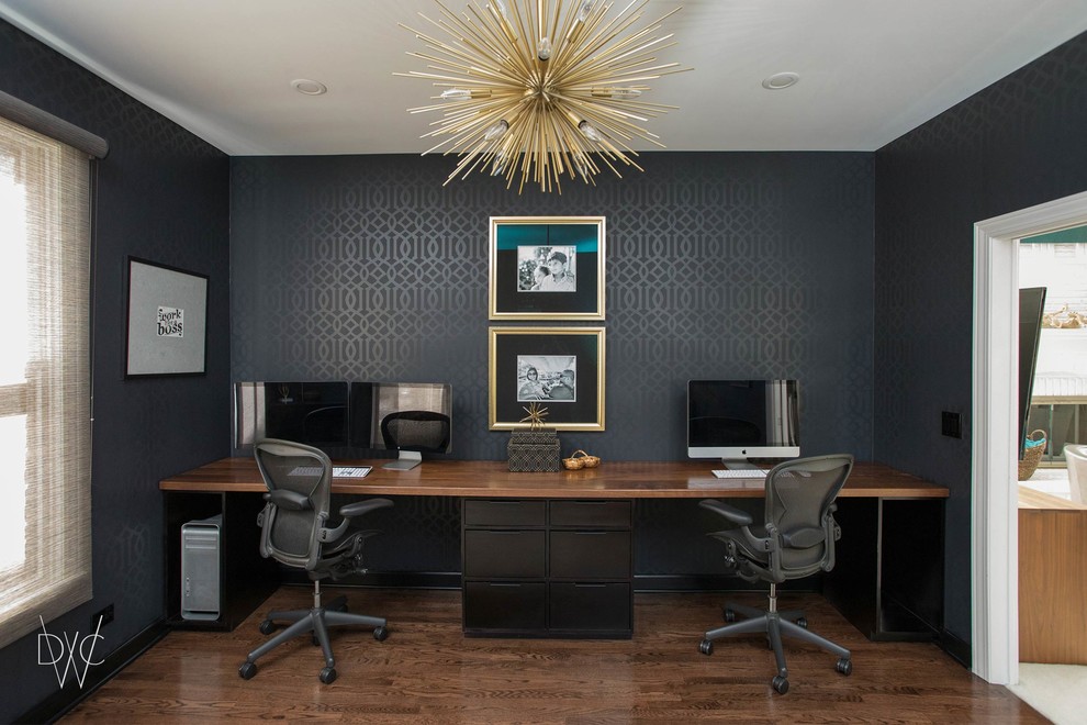 Large trendy built-in desk medium tone wood floor and brown floor home office photo in Chicago with black walls