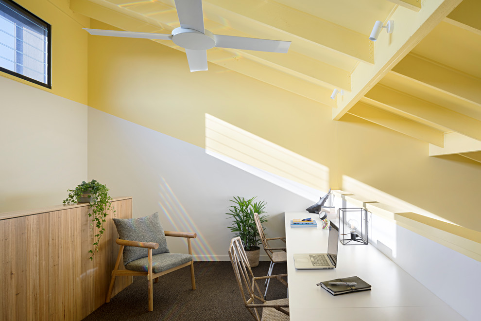 Foto på ett funkis arbetsrum, med gula väggar, heltäckningsmatta, ett inbyggt skrivbord och grått golv