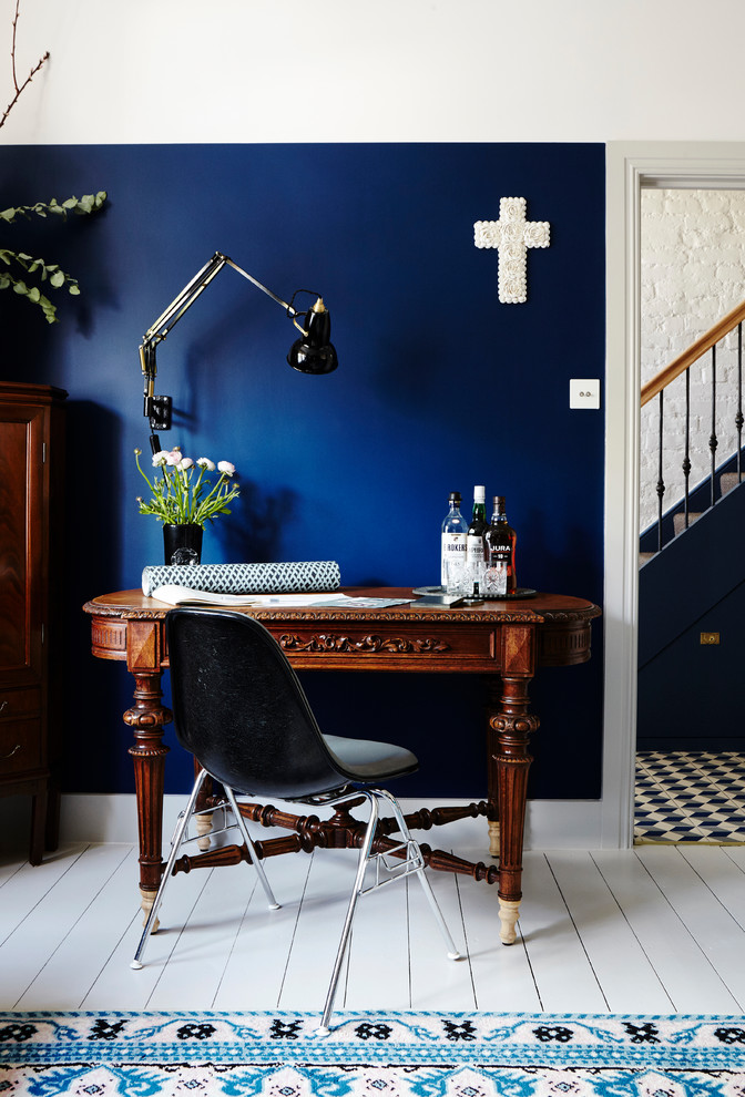 Großes Rustikales Arbeitszimmer mit Arbeitsplatz, blauer Wandfarbe, gebeiztem Holzboden, Kaminofen, Kaminumrandung aus Backstein, freistehendem Schreibtisch und weißem Boden in London