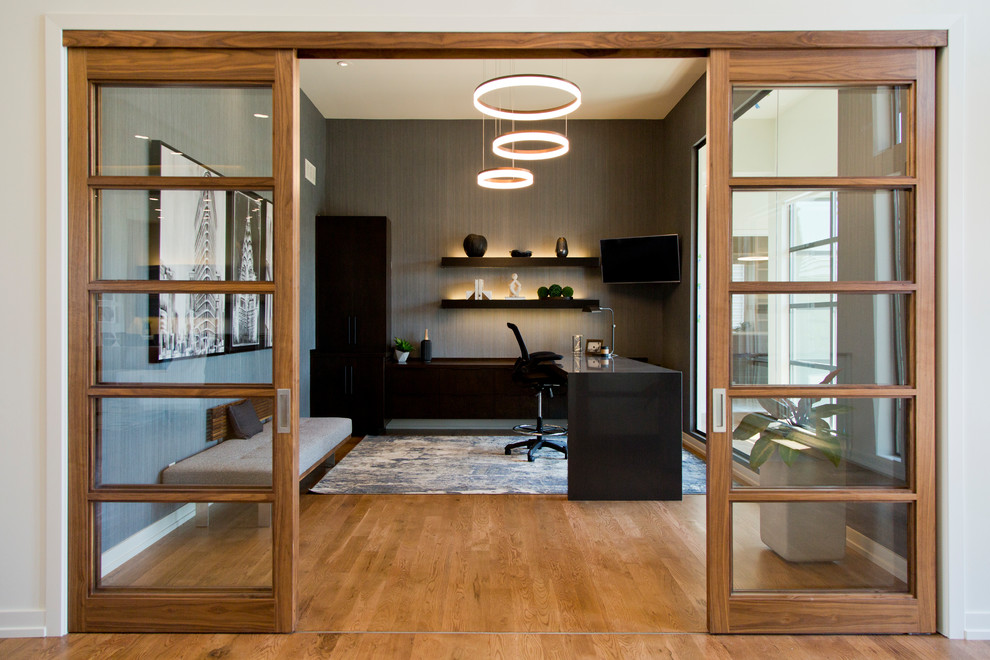 Großes Modernes Arbeitszimmer mit grauer Wandfarbe, braunem Holzboden, Einbau-Schreibtisch und braunem Boden in Kansas City
