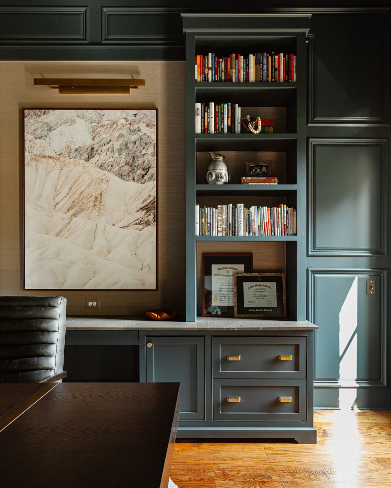 Klassisk inredning av ett mellanstort hemmabibliotek, med gröna väggar, mellanmörkt trägolv, en standard öppen spis, en spiselkrans i sten, ett fristående skrivbord och brunt golv