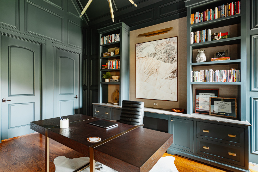 ダラスにある高級な中くらいなトランジショナルスタイルのおしゃれな書斎 (緑の壁、無垢フローリング、標準型暖炉、石材の暖炉まわり、自立型机、茶色い床、三角天井、パネル壁) の写真