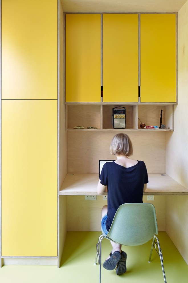 Foto på ett mellanstort funkis hemmabibliotek, med gula väggar och ett inbyggt skrivbord