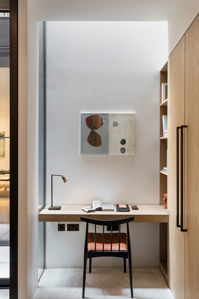 Inspiration for a small contemporary home office in London with white walls, a built-in desk and beige floors.