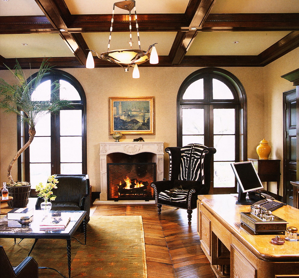 Exemple d'un grand bureau chic avec un mur beige, un sol en bois brun, une cheminée standard, un manteau de cheminée en plâtre, un bureau indépendant et un sol marron.