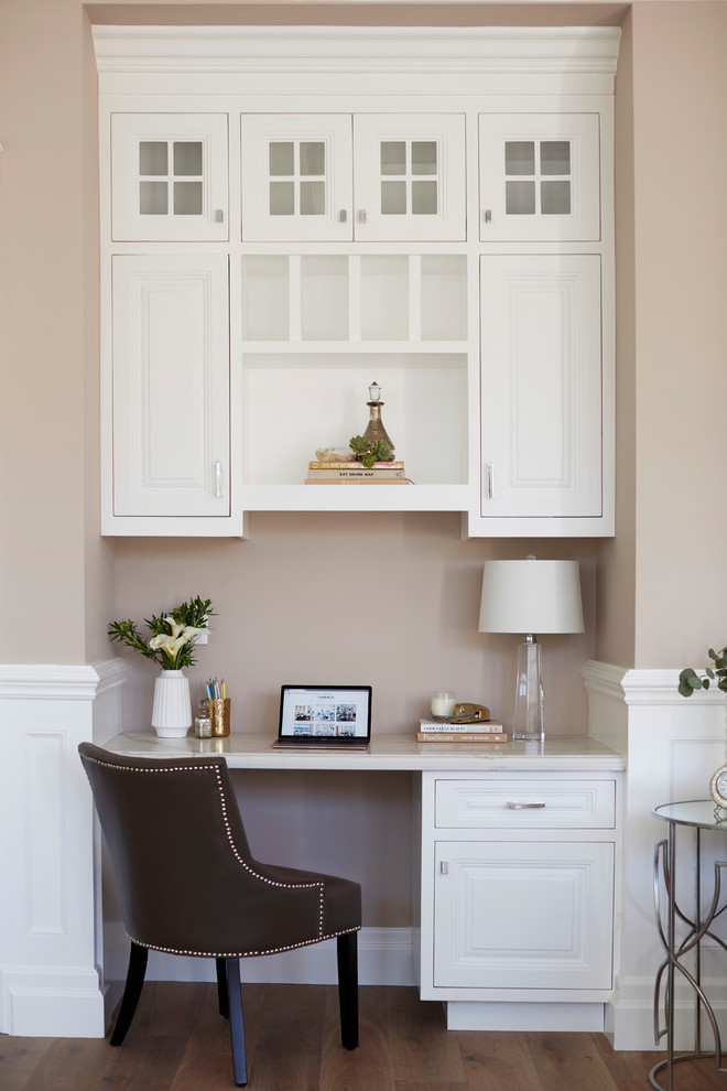 This is an example of a medium sized classic study in Los Angeles with beige walls, medium hardwood flooring, no fireplace, a built-in desk and brown floors.