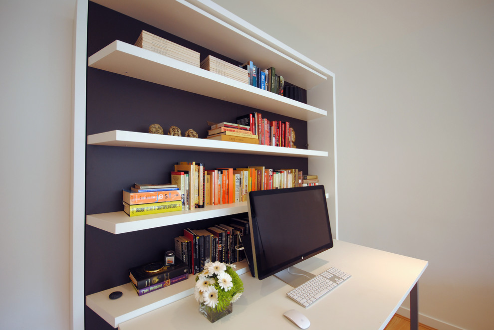 Foto på ett litet funkis hemmabibliotek, med vita väggar, ljust trägolv och ett inbyggt skrivbord