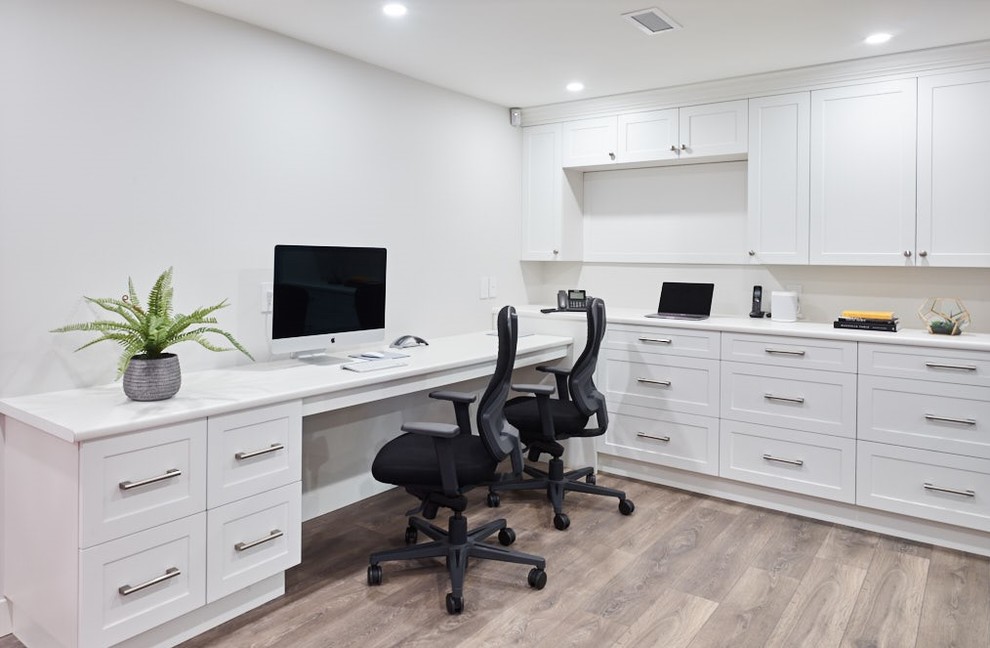 Foto de despacho minimalista de tamaño medio con paredes blancas, suelo de madera en tonos medios, escritorio empotrado y suelo marrón