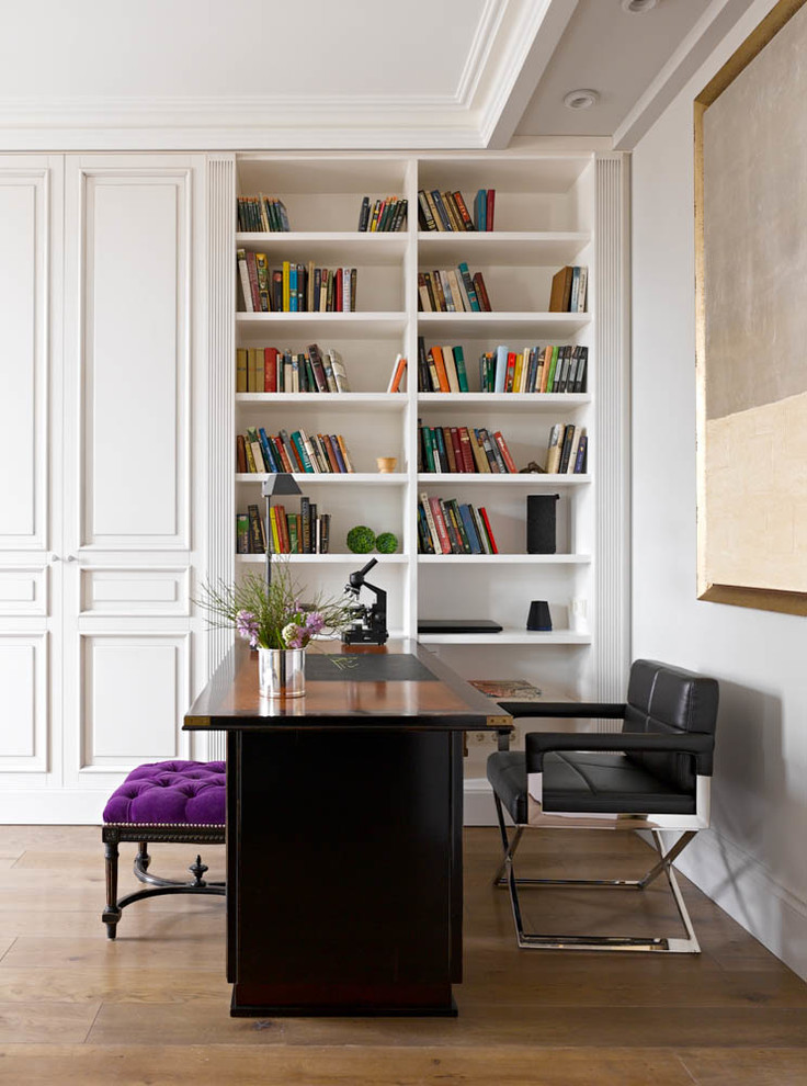 Foto på ett funkis hemmabibliotek, med ett fristående skrivbord, vita väggar och mellanmörkt trägolv