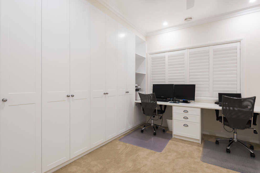 Idee per un grande studio tradizionale con pareti bianche, moquette, scrivania incassata e pavimento beige
