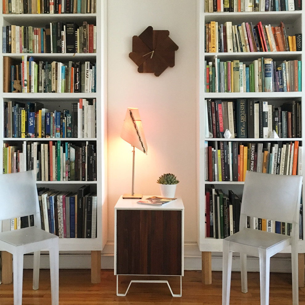 Inredning av ett modernt litet arbetsrum, med ett bibliotek, vita väggar, mellanmörkt trägolv, ett fristående skrivbord och brunt golv
