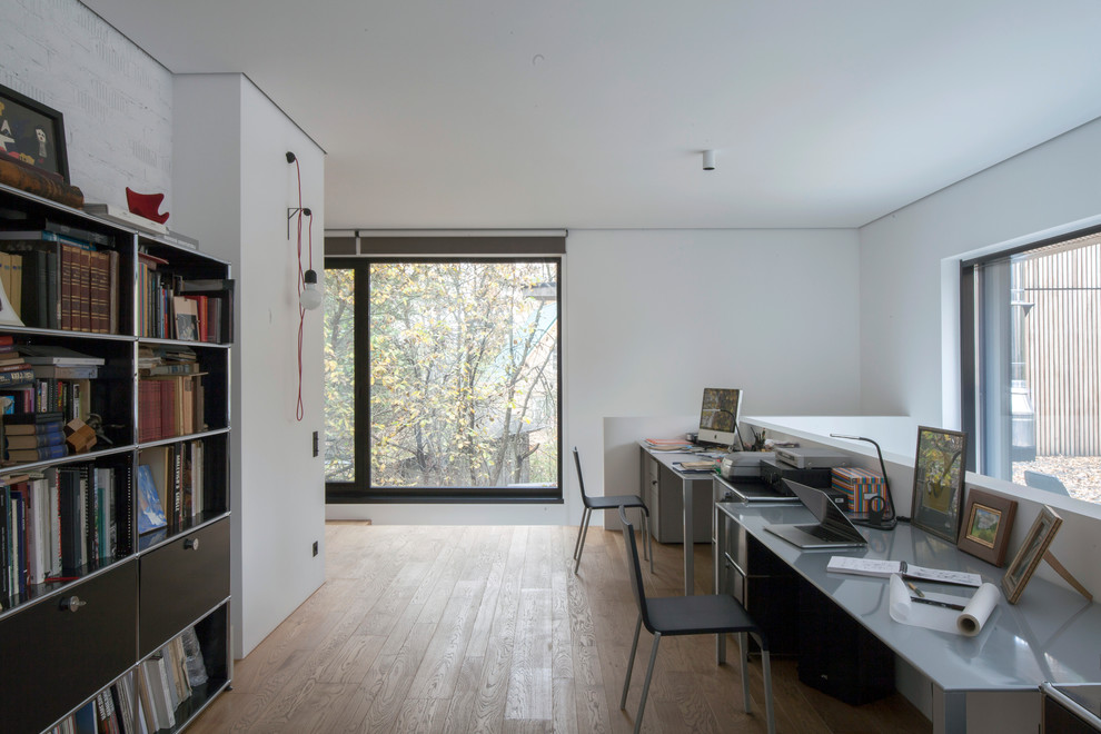 Imagen de despacho minimalista con paredes blancas, suelo de madera en tonos medios, escritorio independiente y suelo marrón
