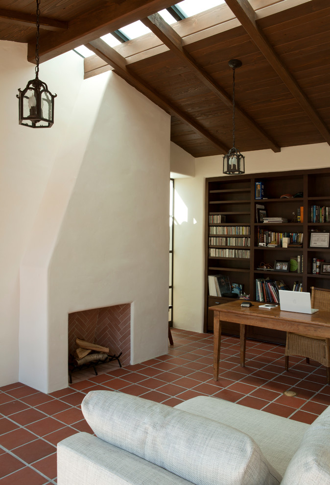 Exempel på ett medelhavsstil hemmabibliotek, med vita väggar, en standard öppen spis och ett fristående skrivbord