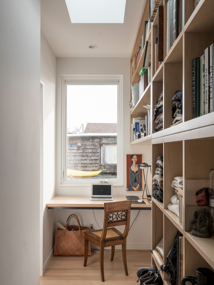 Foto de despacho costero sin chimenea con biblioteca, paredes blancas, suelo de madera clara, escritorio empotrado y suelo beige