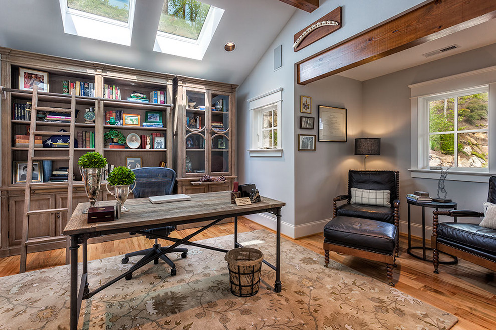 Ejemplo de despacho clásico grande sin chimenea con biblioteca, paredes grises, suelo de madera en tonos medios y escritorio independiente