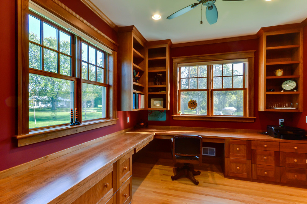 Cette photo montre un bureau craftsman avec un mur rouge, parquet clair et un bureau intégré.