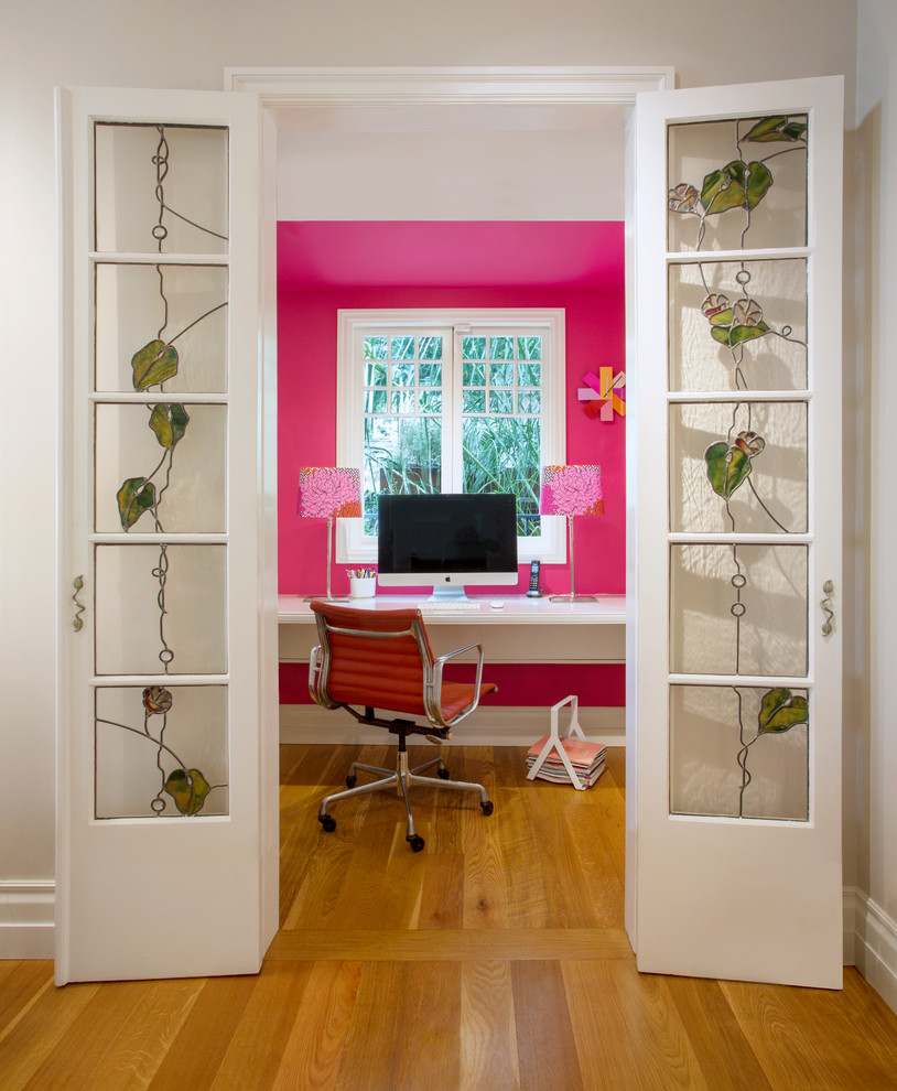 Стильный дизайн: рабочее место в современном стиле с розовыми стенами, паркетным полом среднего тона, отдельно стоящим рабочим столом и коричневым полом - последний тренд