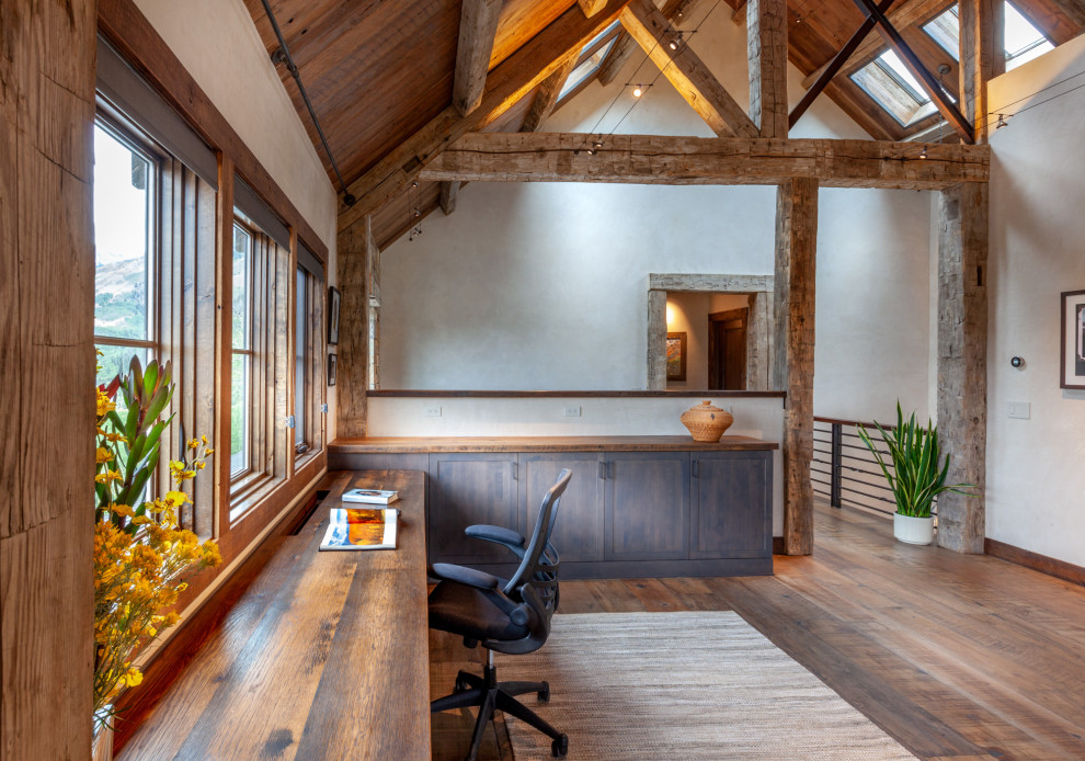 Idées déco pour un grand bureau montagne avec un mur blanc, un sol en bois brun, un bureau intégré et un sol marron.