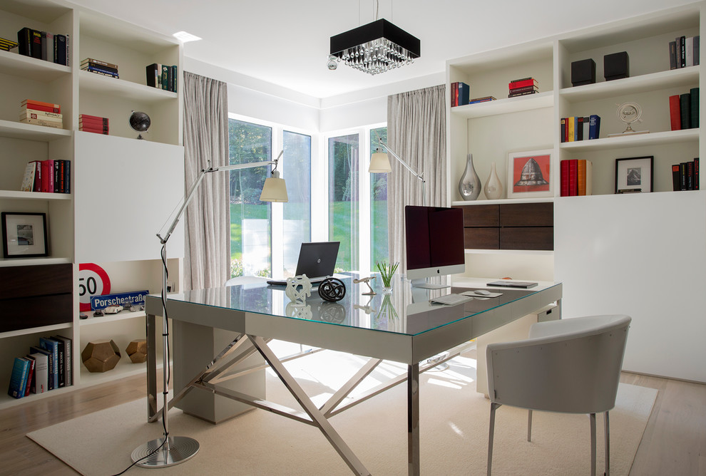 Modelo de despacho minimalista de tamaño medio sin chimenea con paredes blancas, suelo de madera clara y escritorio independiente