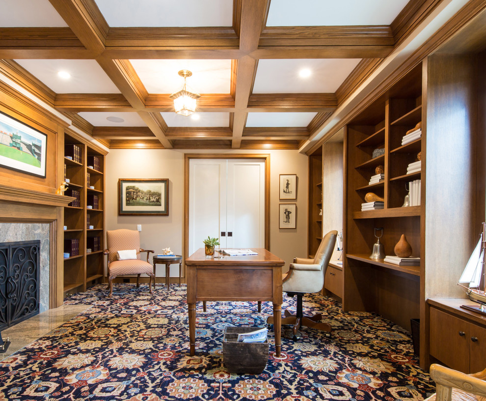 Großes Klassisches Arbeitszimmer mit Arbeitsplatz, beiger Wandfarbe, Teppichboden, Kamin, Kaminumrandung aus Stein, freistehendem Schreibtisch und buntem Boden in San Diego