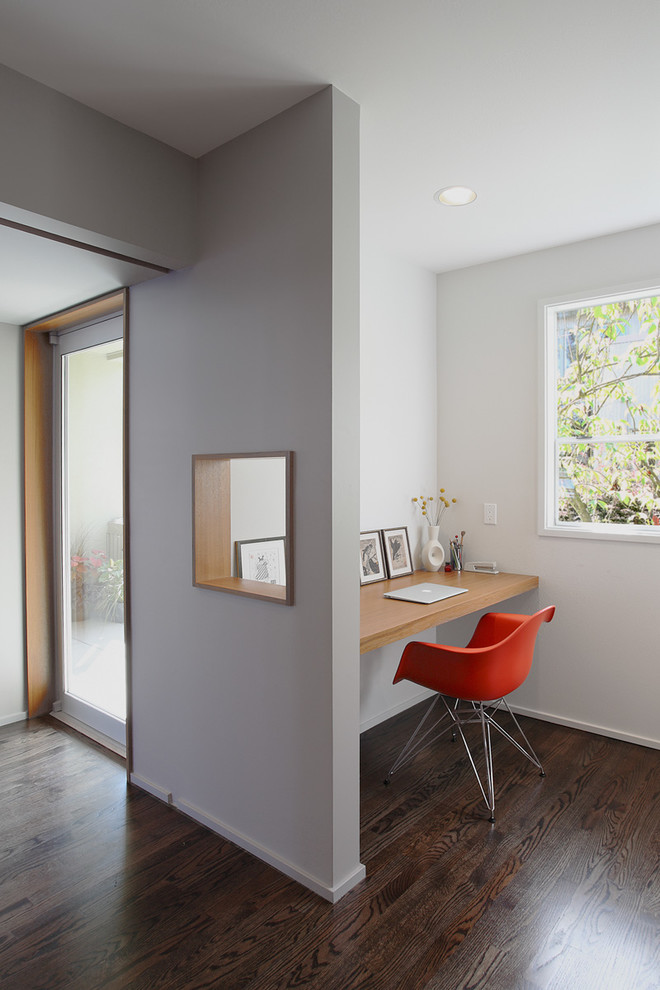 Diseño de despacho retro pequeño con paredes blancas, suelo de madera oscura y escritorio empotrado