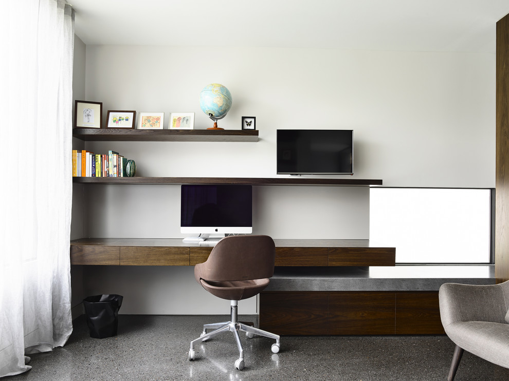 Diseño de despacho moderno con paredes blancas, suelo de cemento y escritorio empotrado
