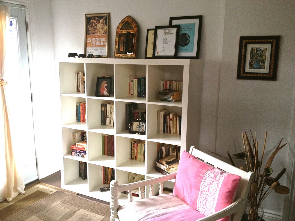 Foto på ett litet eklektiskt hemmabibliotek, med vita väggar, mörkt trägolv och ett fristående skrivbord