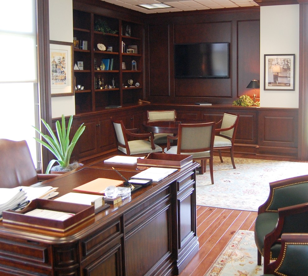 Klassisk inredning av ett stort arbetsrum, med mellanmörkt trägolv, ett fristående skrivbord och brunt golv